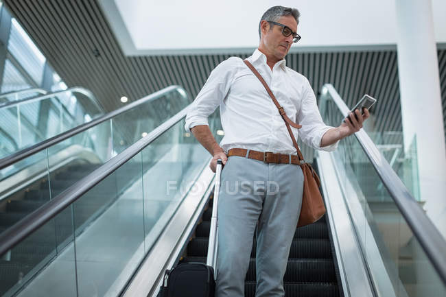 Vue basse de l'homme d'affaires concentré vérifiant son téléphone portable sur l'escalator dans le bureau — Photo de stock