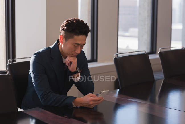Vista lateral do empresário sentado usando telefone celular na sala de conferências no escritório — Fotografia de Stock
