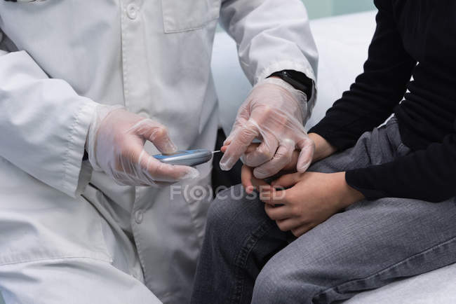 Media sección de joven asiático médico masculino examinando caucásico niño paciente con glucosímetro en clínica - foto de stock