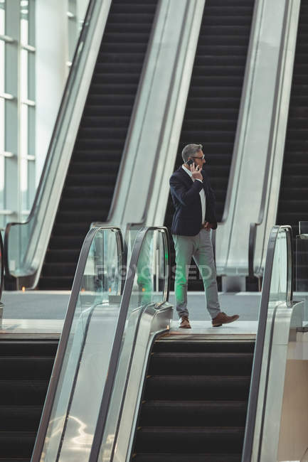 Far sight of businessman talking on the phone on escalator in office — Stock Photo