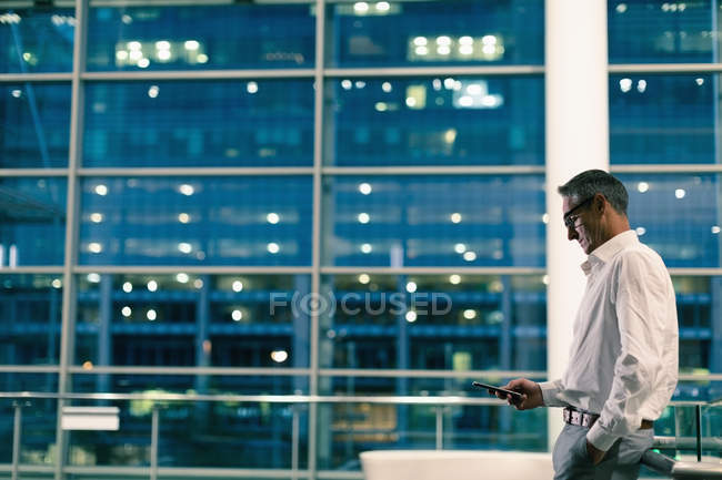 Вид збоку бізнесмена, використовуючи свій мобільний телефон проти офісної будівлі за ніч — стокове фото