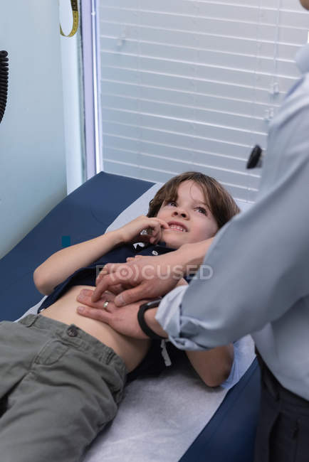 Vue latérale de jeune asiatique mâle médecin examen caucasien garçon patient avec la main dans une clinique — Photo de stock