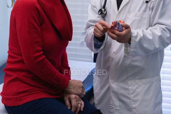 Section MId du jeune médecin asiatique et patient âgé discutant sur le modèle cardiaque à la clinique — Photo de stock