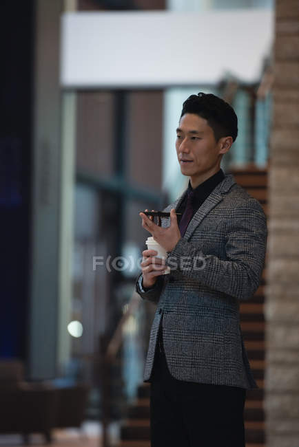 Side view of businessman talking on mobile phone while having coffee in the modern office — Stock Photo