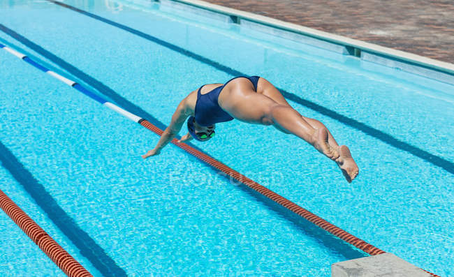 Vista alta di giovane nuotatrice caucasica che salta in acqua di una piscina sotto il sole — Foto stock
