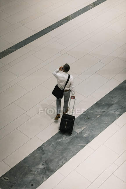 Erhabener Blick auf Geschäftsmann mit Reisekoffer, der auf dem Flur mit dem Handy telefoniert — Stockfoto