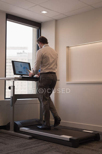 Side view of businessman working while exercising on treadmill in the modern office — Stock Photo