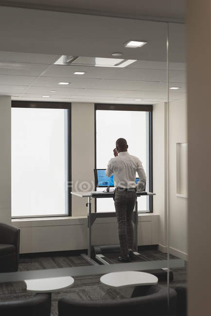 Empresário falando no celular enquanto se exercita na esteira rolante no escritório — Fotografia de Stock