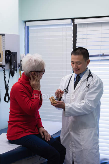 Vista frontale del giovane medico maschio asiatico e paziente anziano che discute sul modello di orecchio in clinica — Foto stock
