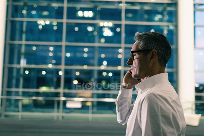 Seitenansicht eines Geschäftsmannes, der nachts vor einem Bürogebäude telefoniert — Stockfoto