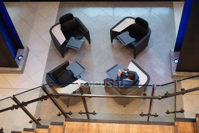 Вид сверху на бизнесмена, использующего мобильный телефон, сидящего в кресле в холле офиса — стоковое фото