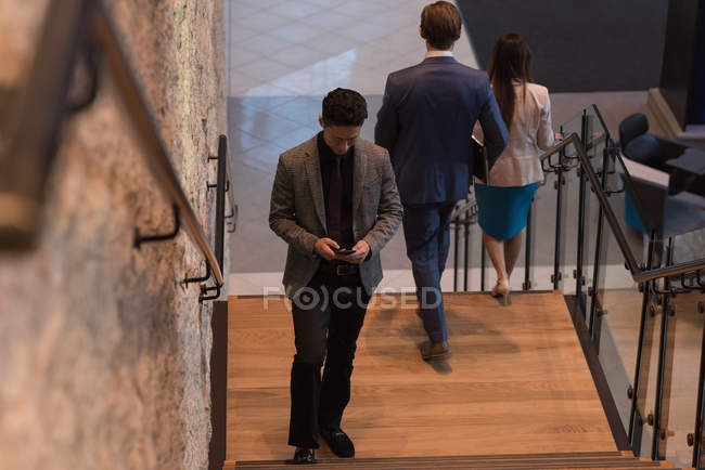 Vorderseite des Geschäftsmannes mit Handy im modernen Büro mit Menschen im Hintergrund — Stockfoto