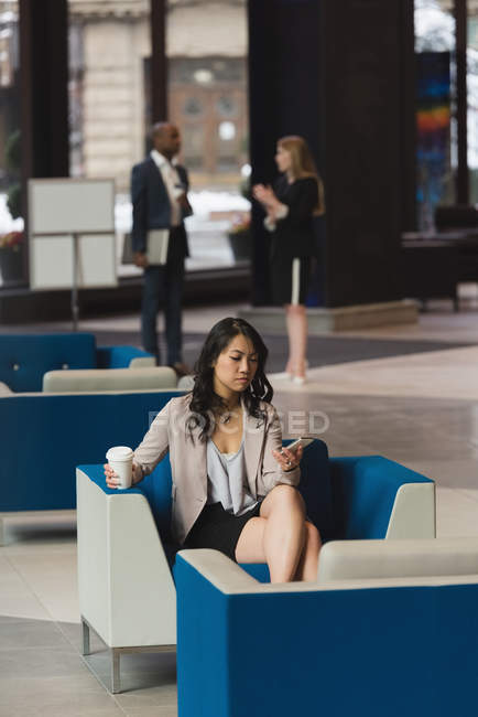 Vista lejana de la mujer de negocios utilizando el teléfono móvil en el vestíbulo en la oficina - foto de stock