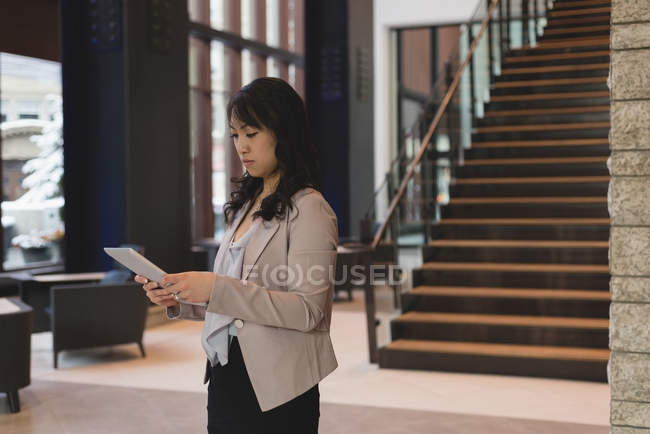 Vista lateral de la mujer de negocios de pie utilizando la mesa digital en el vestíbulo de la oficina moderna - foto de stock