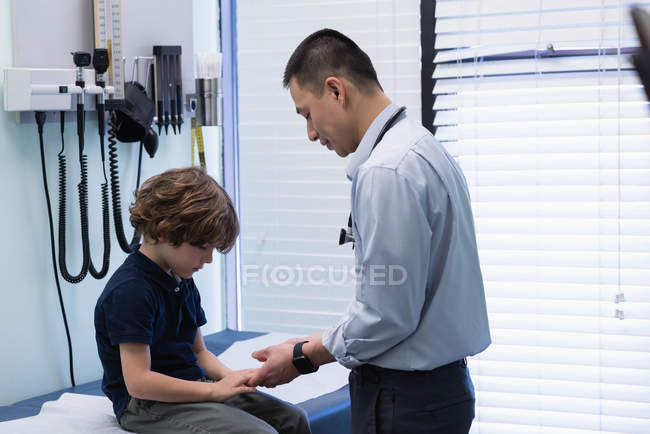 Вид сбоку на молодого врача-азиата, осматривающего пациента кавказского мальчика в клинике — стоковое фото