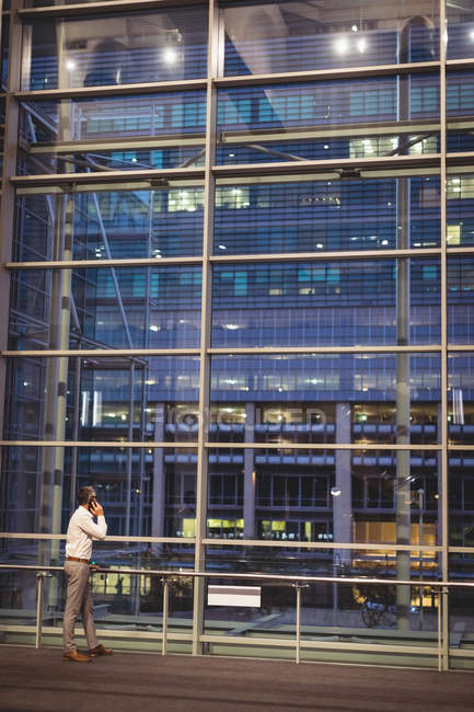 Rear view of businessman talking on the mobile phone while looking at a building through windows by night — Stock Photo