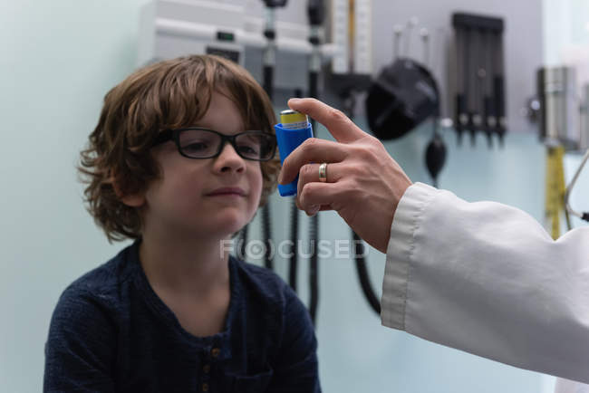 Front view of young asian male doctor helping a caucasian boy patient in using asthma inhaler in clinic. Male doctor holding asthma inhaler. Male doctor interacting with patient — Stock Photo