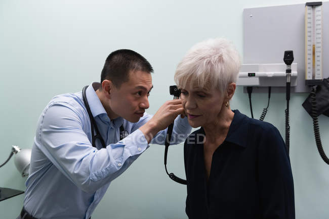 Visão frontal do jovem médico asiático examinando um paciente sênior na clínica — Fotografia de Stock