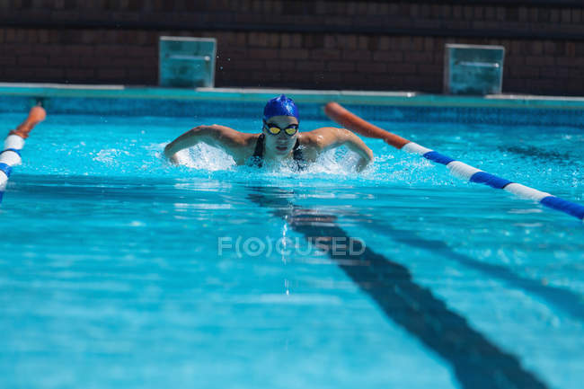 Vista frontal de una joven nadadora con gafas de natación nadando en la piscina - foto de stock