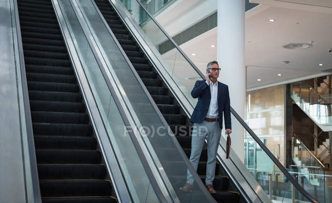 Vista frontal del hombre de negocios hablando en el teléfono móvil en la escalera mecánica en la oficina - foto de stock