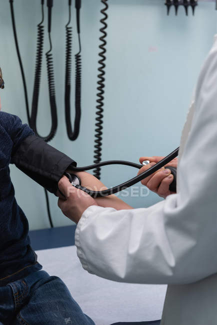 Visão lateral de jovem asiático médico masculino verificando a pressão arterial de caucasiano menino paciente na clínica — Fotografia de Stock