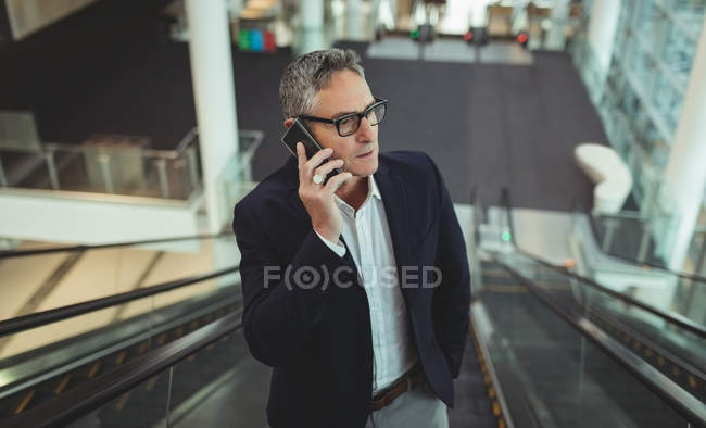 Vista anteriore dell'uomo d'affari che parla sul telefono cellulare sulla scala mobile in ufficio — Foto stock