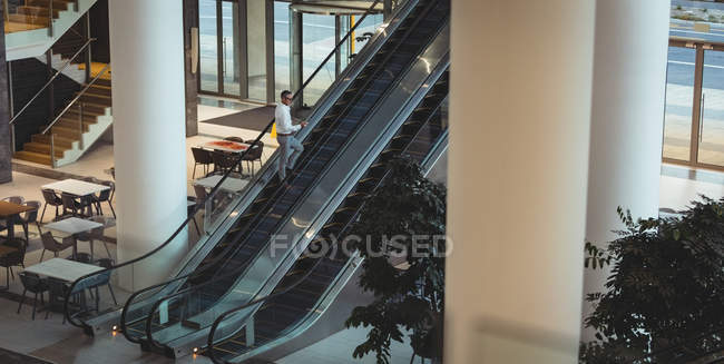 Підвищений вигляд бізнесмена, який дивиться на свій смартфон на ескалаторі у порожньому офісі — стокове фото