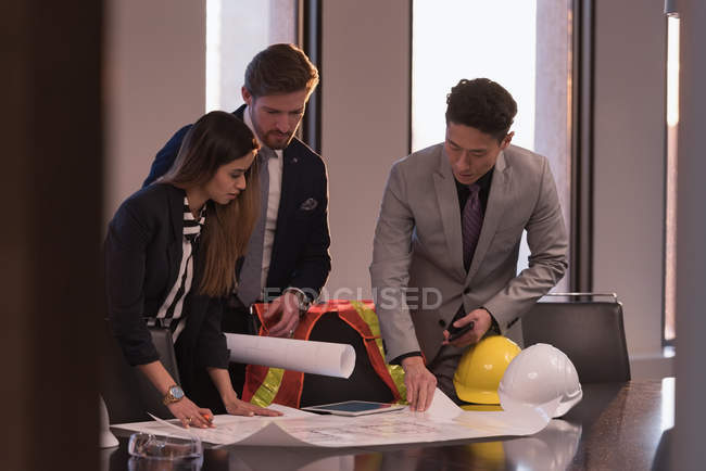 Side view of business people discussing over blueprint in the conference room surrounded of safety objects at workplace — Stock Photo
