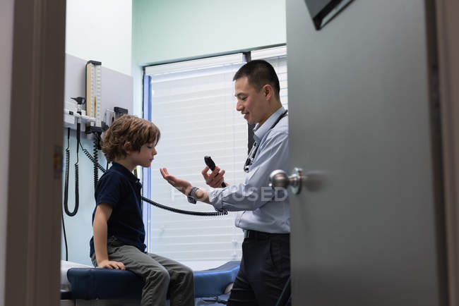 Jeune asiatique mâle médecin examiner un caucasien garçon patient avec outil médical dans clinique — Photo de stock