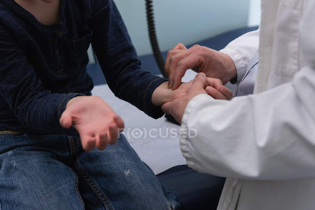 Vista laterale del giovane medico maschio asiatico che controlla il polso del paziente caucasico del ragazzo in clinica — Foto stock