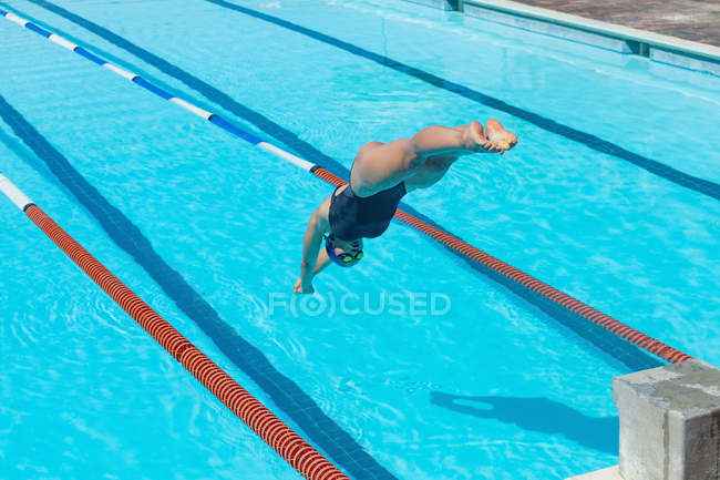 Hohe Ansicht einer jungen kaukasischen Schwimmerin, die in der Sonne ins Wasser eines Schwimmbades springt — Stockfoto