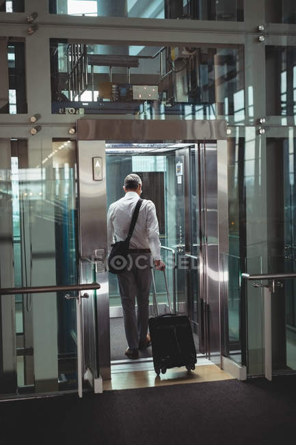 Вид сзади бизнесмена с дорожной сумкой, входящего в лифт в офисе — стоковое фото