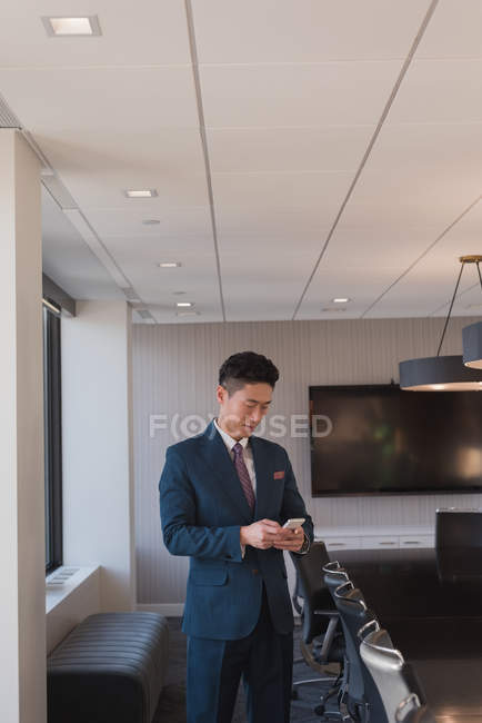 Вид сбоку стоящего бизнесмена с помощью мобильного телефона в конференц-зале в офисе — стоковое фото
