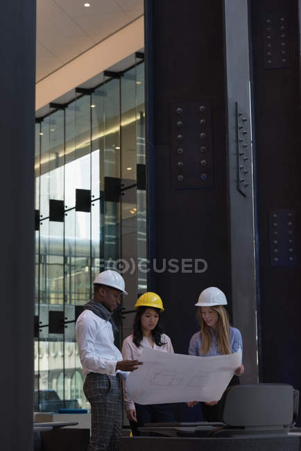 Side view of group of architects discussing over blueprint in the modern office. They are equipped with safety helmets — Stock Photo