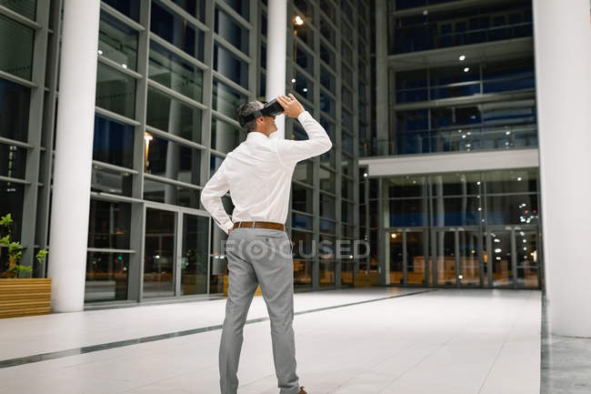 Вид ззаду бізнесмена, який відчуває гарнітуру VR за межами офісу вночі — стокове фото