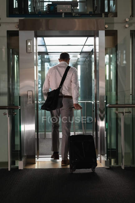 Visão traseira do homem de negócios com saco de viagem entrando no elevador no escritório — Fotografia de Stock