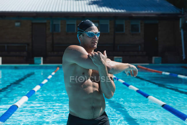 Frontansicht eines jungen männlichen Schwimmers mit Schwimmbrille, der sich im Schwimmbad ausstreckt — Stockfoto
