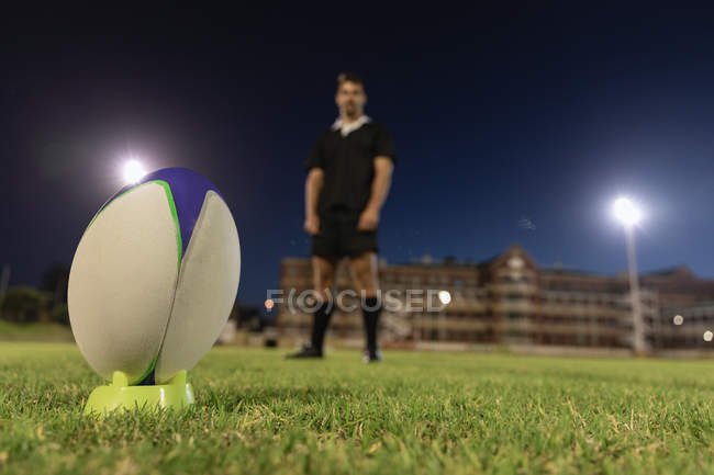 Vista de baixo ângulo de um jogador de rugby masculino em pé e esperando para chutar a bola de rugby no estádio à noite — Fotografia de Stock