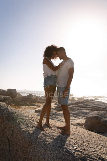 Seitenansicht eines afrikanisch-amerikanischen Paares in romantischer Stimmung, das auf einem Felsen am Meer steht und einander anschaut — Stockfoto