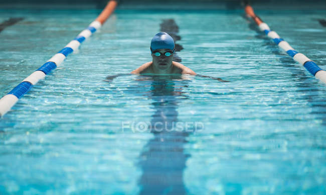 Vista frontal de un joven nadador masculino caucásico nadando mariposa en la piscina al aire libre bajo el sol - foto de stock