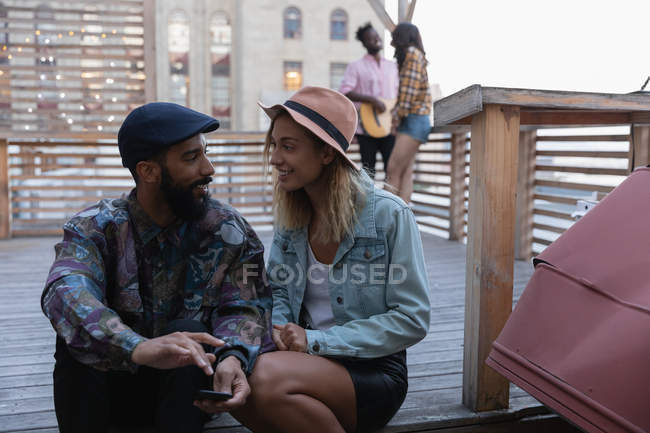 Вид спереду багатонаціональна пара сидить і розмовляє один з одним на балконі вдома — стокове фото