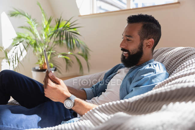 Side view of African american man smiling and using digital tablet at home — Stock Photo