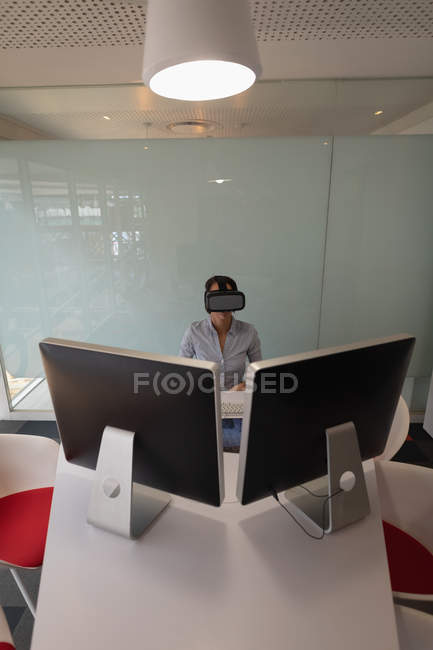 Visão de alto ângulo de uma empresária asiática usando um fone de ouvido de realidade virtual na mesa no escritório — Fotografia de Stock