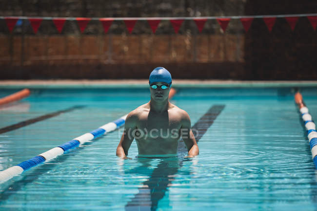 Front view of young Caucasian male swimmer standing in outdoor swimming pool on sunny day — Stock Photo
