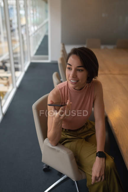 Visão de alto ângulo de uma empresária asiática conversando em seu telefone celular enquanto sentada no escritório — Fotografia de Stock