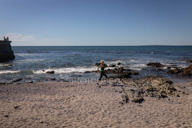 Side view of an active senior woman doing jogging on the beach under the sunshine — Stock Photo