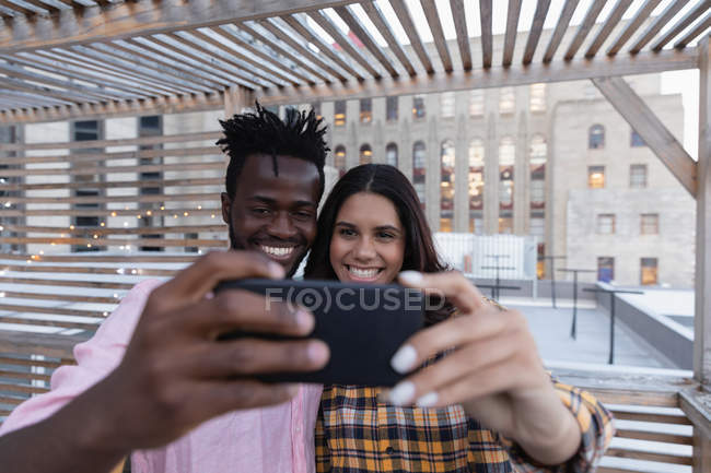 Vista frontal do casal multi étnico tirar selfie na varanda em casa — Fotografia de Stock
