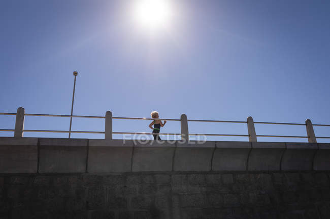 Низкий угол обзора активной пожилой женщины, делающей пробежку на набережной под солнцем — стоковое фото