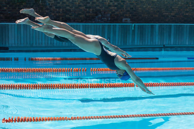 Side view of male and female Caucasian swimmers jumping into water in the same time at the swimming pool in the sunshine — Stock Photo