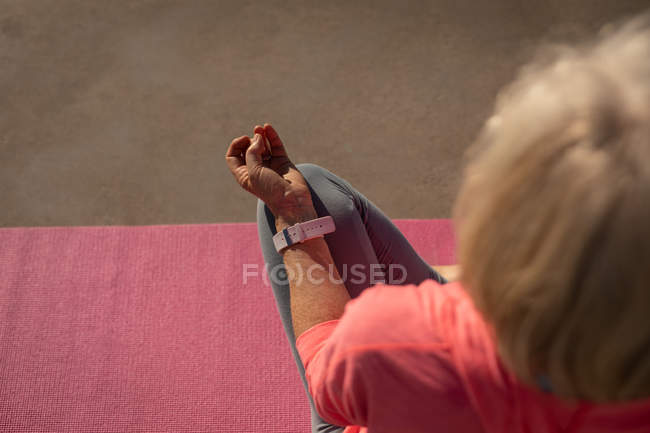 High angle view of an active senior woman performing yoga on a fitness map on a promenade under the sun — Stock Photo